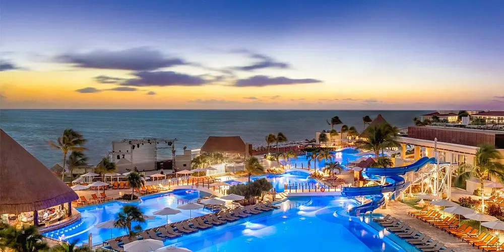 Moon Palace Cancun pools and waterslide glowing at sunset beside the Caribbean Sea